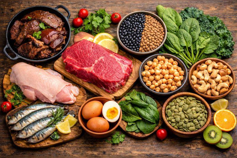 Healthy selection of brain-friendly foods including salmon, blueberries, leafy greens, eggs, nuts and dark chocolate arranged on a wooden table.
